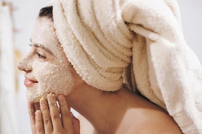 Kobieta z ręcznikiem na głowie nakładająca na twarz peeling