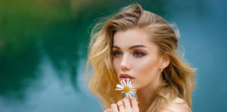 Piękna blondynka z kwiatem w dłoni na tle jeziora